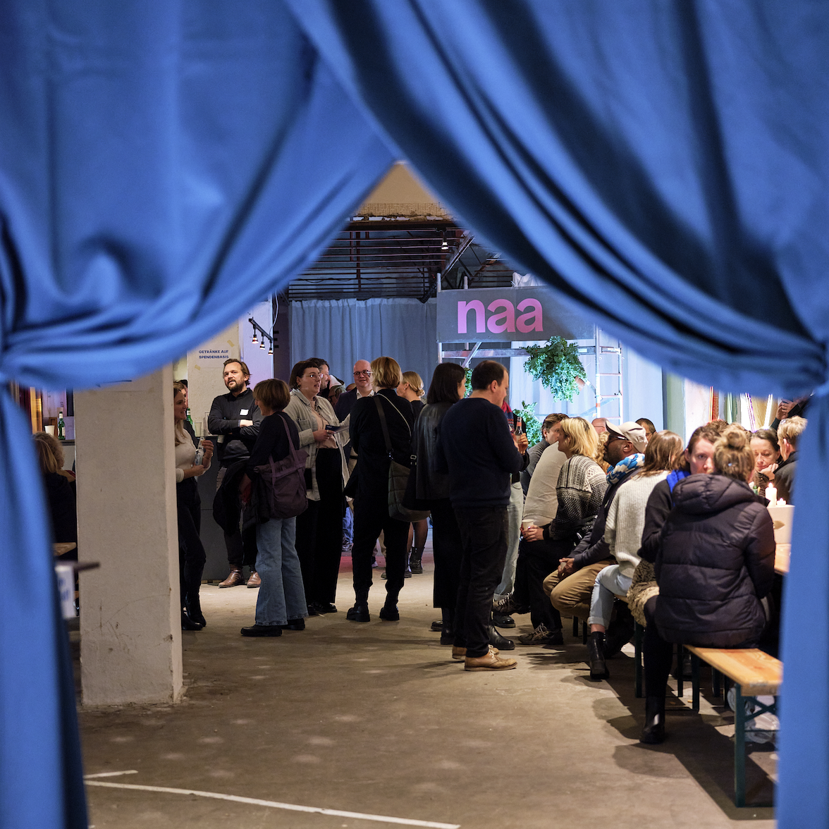 Festliche NAA-Veranstaltung mit zahlreichen Menschen hinter einem Vorhang, die sich unterhalten